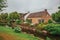 Charming small canal next to rustic houses with lush flowery garden and lawn in cloudy day at Drimmelen.