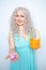 Charming smiling blonde teenager stands in a blue dress with an orange basket with painted eggs for Easter alone on white studio s