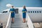 Charming stewardesses standing on airplane stairs under blue sky