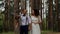 Charming stylish groom walking with his bride in a luxurious pine forest. Talking to each other and laugh.
