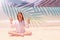 Charming teenager girl in a white shirt and with long hair meditates in a lotus position on the beach. The concept of children`s