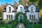 A charming white cottage house with contrasting black trim and a beautiful arched green door. Surrounded by a lush garden and