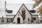 Charming white painted brick cottage with copper accents during snowfall with autumn leaves still on trees