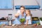Charming woman and little girl taking selfie in modern kitchen, holding bowl of vegetable salad and posting photo in social