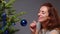 Charming woman with long brown hair and red lips enjoying the process of decorating Christmas tree, smiling woman