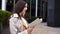 Charming woman is reading book standing on street in city, thoughtful and lovely