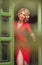 Charming young blonde with red dress posing in a green painted door frame. Sensual gorgeous young woman in red outfit with Marilyn