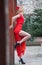 Charming young blonde in red dress with red flower in hair posing against wooden wall.Sensual gorgeous young woman