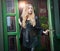 Charming young blonde woman in black outfit posing in a green painted door frame. gorgeous young woman with long curly hair