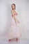 A charming young caucasian girl stands in a pink long prom dress with flower petals on her chest and poses on a white background i