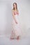 A charming young caucasian girl stands in a pink long prom dress with flower petals on her chest and poses on a white background i