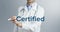 A charming young doctor writes and underlines the importance of the word Certified on a neutral background with a blue marker