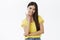 Charming young and friendly dark-haired female in trendy yellow t-shirt crossing one arm over chest touching skin gently