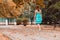 Charming young girl in blue dress walks in autumn park. Back view. Lonely blonde lady with loose hair. Autumn fallen gold leaves