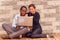 Charming young interracial couple sitting by brick wall with laptop interacting and having fun