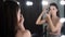 Charming young woman model applies dark shadows to her face near mirror