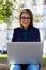 Charming young woman using laptop gadget sitting outdoors at sunny beautiful day