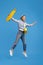 Charming young woman with yellow penny or skate board dancing over blue background.