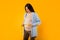 Charting the growth. Young pregnant woman measuring belly at last trimester of pregnancy, posing over yellow background