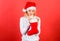 Check contents of christmas stocking what she received. Woman in santa hat unpacking christmas gift red background