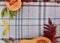 checkered beige autumn background with edible cut pumpkin and crimson yellow leaves