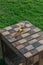 A checkered wood box is being used as a table, on its surface there is a cup full of beer and its shadow, the table is