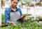 Checking the growth in greenhouse. Girl in apron with tablet caring for flowers