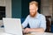 Cheeful red-haired hipster man looking using laptop computer for remote work