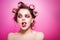 Cheeky girl posing on pink background in body, with curlers on head. Pretty woman with sweet makeup in studio