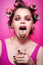 Cheeky girl with sweets on tongue and glass with candies posing on pink background in body, with curlers on head. Pretty sexy