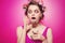 Cheeky girl with sweets on tongue and glass with candies posing on pink background in body, with curlers on head. Pretty sexy