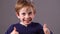 Cheeky young preschool red hair boy with freckles showing his excitement with double thumbs up, grey background studio