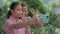 Cheerful adorable Asian girl holding smartphone for filming video with happy senior grandmother in the home garden.