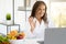 Cheerful adult caucasian nutritionist doctor in white coat at table with fruits waving hand in laptop