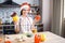 Cheerful adult woman stand in kitchen and posing on camera. Red hat on head. Hold colorful peppers in hands. Cooking and