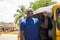 cheerful african man standing next to his tuk tuk taxi smiling