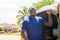 cheerful african man standing next to his tuk tuk taxi smiling