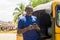 cheerful african man standing next to his tuk tuk taxi smiling and using his smart phone