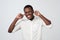 Cheerful african man in white shirt plugging ears with fingers and winking.