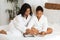 Cheerful African Mom And Daughter Reading Beauty Magazine At Home, Wearing Bathrobes