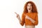 Cheerful amused attractive redhead woman with blue eyes, curly hair pointing left blank space, checking out cool promo