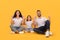 Cheerful Arabic Family Pointing Fingers Up Sitting Over Yellow Background