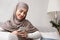 Cheerful arabic girl in hijab spending time with smartphone at home