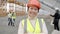 Cheerful Asian construction worker wearing uniform smiling at construction site while people working in background