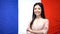 Cheerful Asian girl standing with hands crossed against French flag background