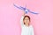 Cheerful asian little child girl raise up a blue toy airplane flying on air isolated on pink background