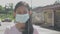 Cheerful Asian long hair pretty girl in protective mask wearing earphones standing on the street in residential area.