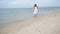 Cheerful asian woman barefoot walking on tropical summer beach. Woman walking along wave of sea water and sand on the beach. Enjoy