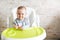 Cheerful baby child eats food itself with spoon. Portrait of happy kid in high chair in sunny kitchen. background with copy space