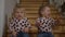 Cheerful baby twins sitting on stairs at home laughing gesturing in slow motion. Portrait of joyful positive happy